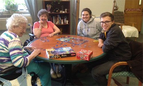 Students helping nursing home residents with jig-saw puzzle.